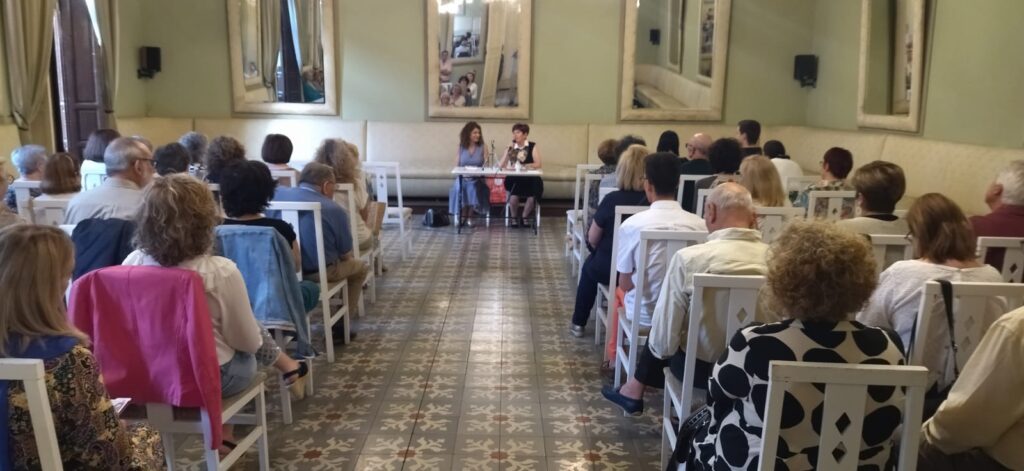Panorámica del salón de baile del Casino de Mula. En primer plano, los asistentes al acto. Al fondo, Consuelo Martínez, la profesora de literatura que realizó la presentación y a su lado, la autora del libro.